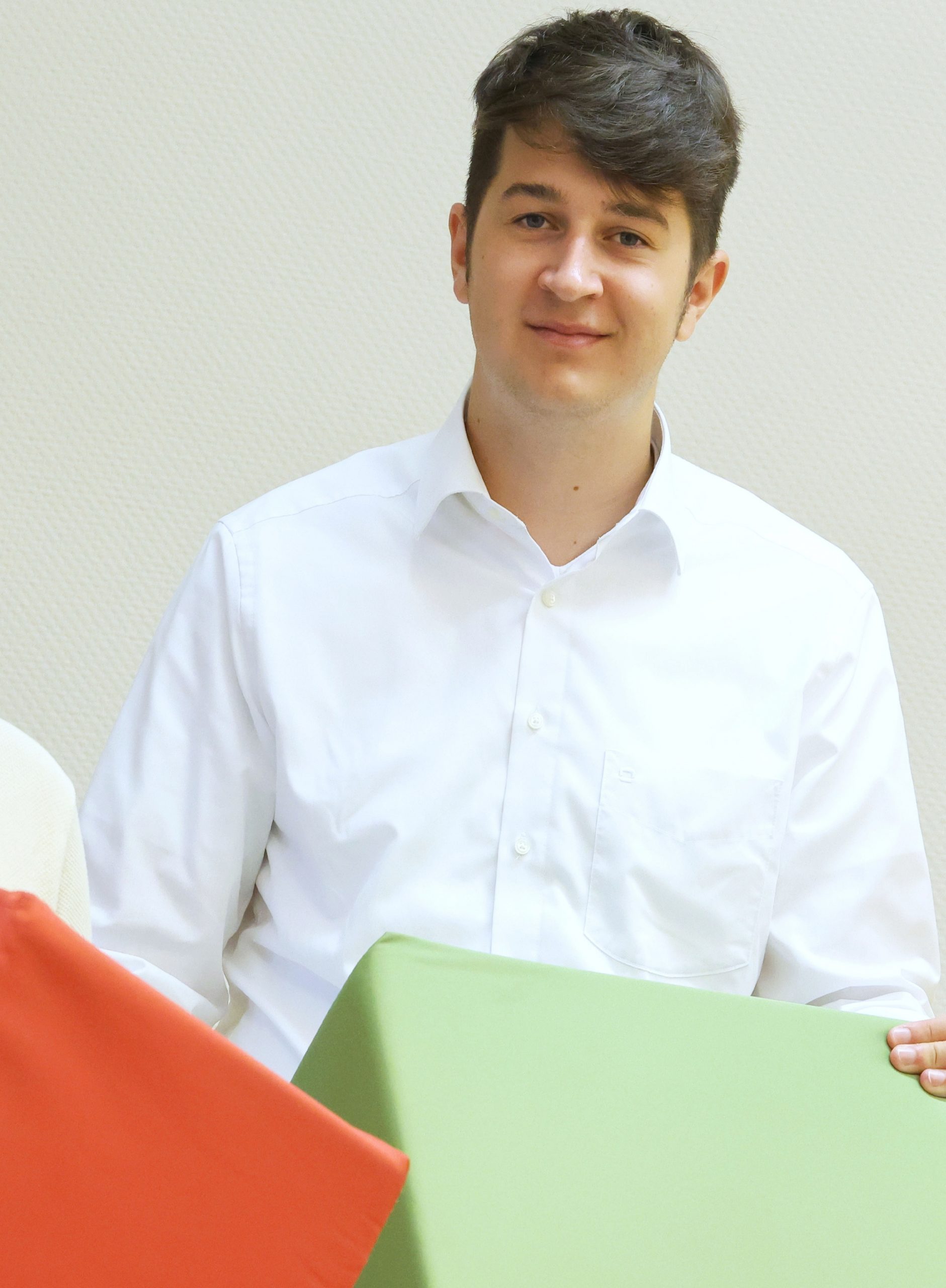 Junger Mann mit dunkelbraunen Haaren trägt ein weißes Hemd